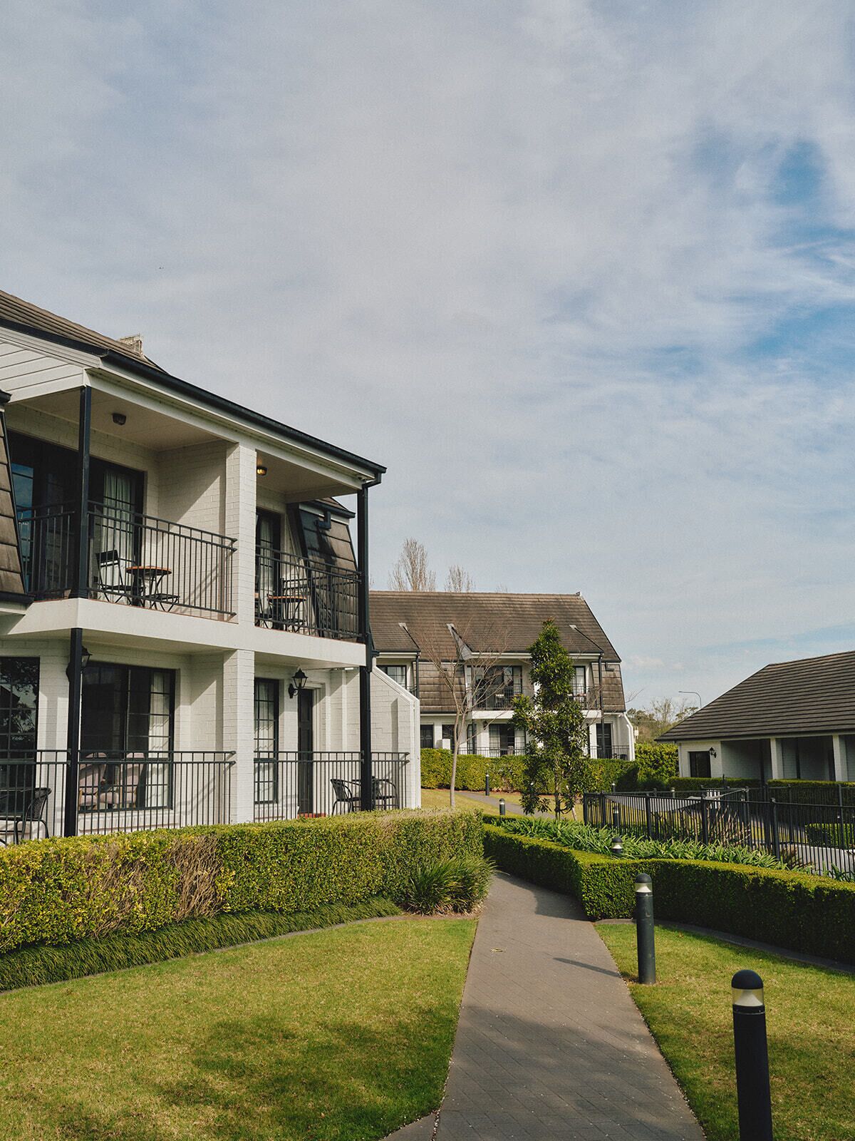 A residential building with a covered walkway, multiple balconies, and a well-maintained lawn.