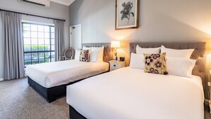 A hotel room with two beds, a large window with curtains, a framed floral artwork, and a bedside table with a lamp. - Camden Valley Inn (Cawdor)