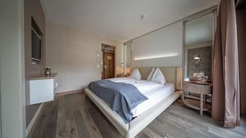 A modern hotel room with a large bed, a bedside table, a mirror, and a small desk with a lamp.