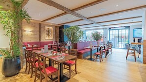 A restaurant with wooden beams, red cushioned seating, and large windows.