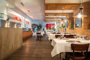 Restaurante com vigas de madeira no teto, toalhas de mesa brancas e luminárias pendentes.