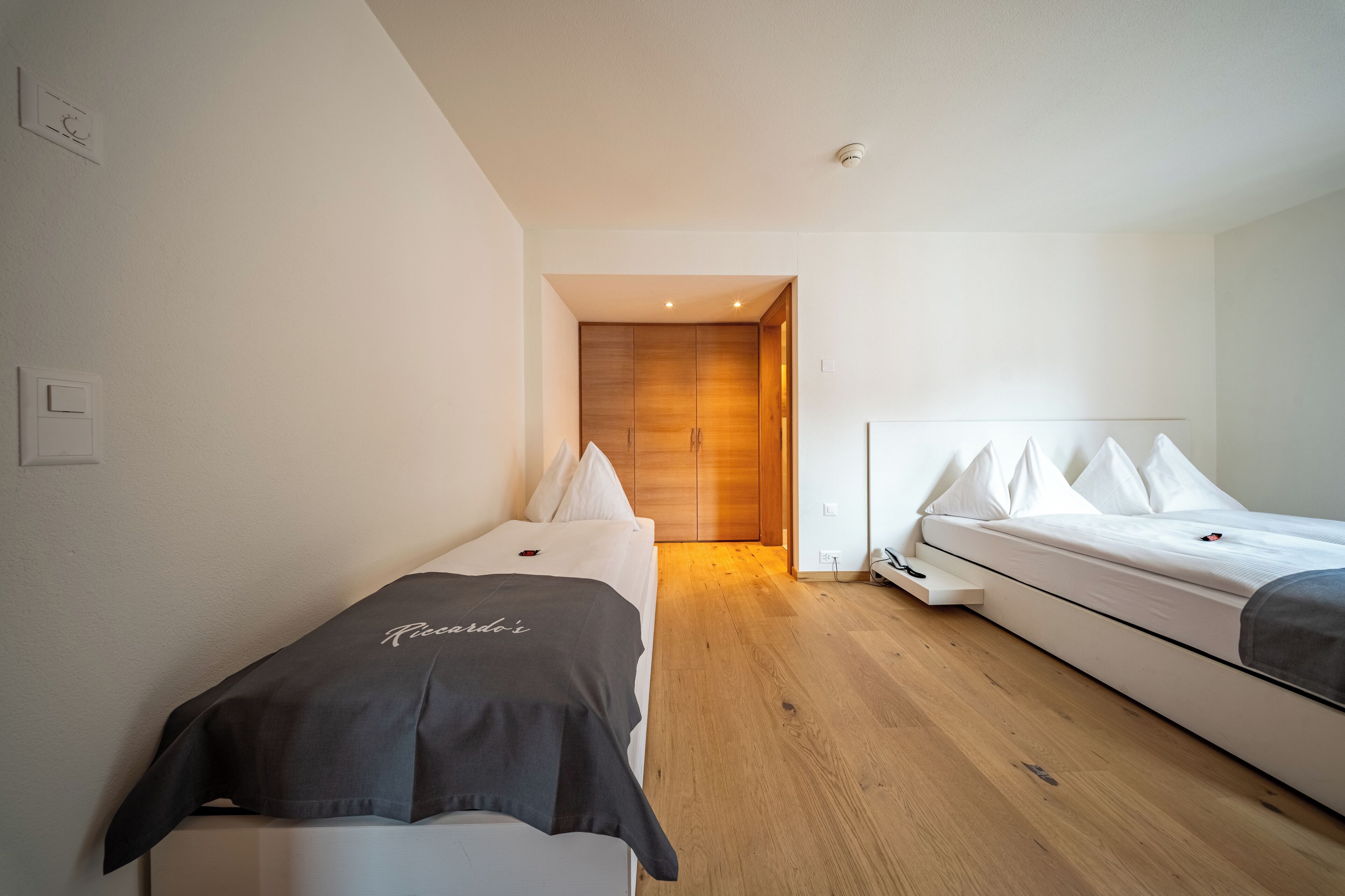 Een moderne hotelkamer met een houten vloer, een bed met wit beddengoed, een nachtkastje en een kledingkast.