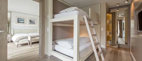 Habitación con literas de madera, una cama individual y un baño visible a través de una puerta abierta.