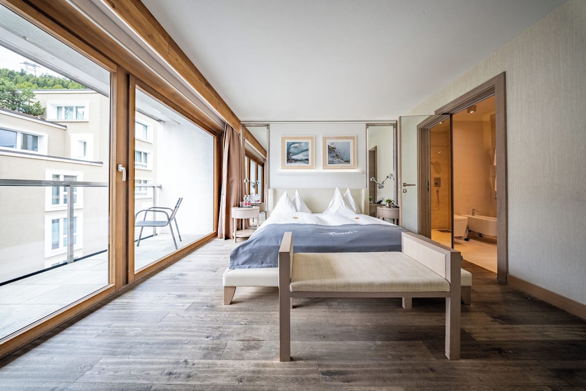 A modern bedroom with a large bed, a bench, and a view of a balcony.