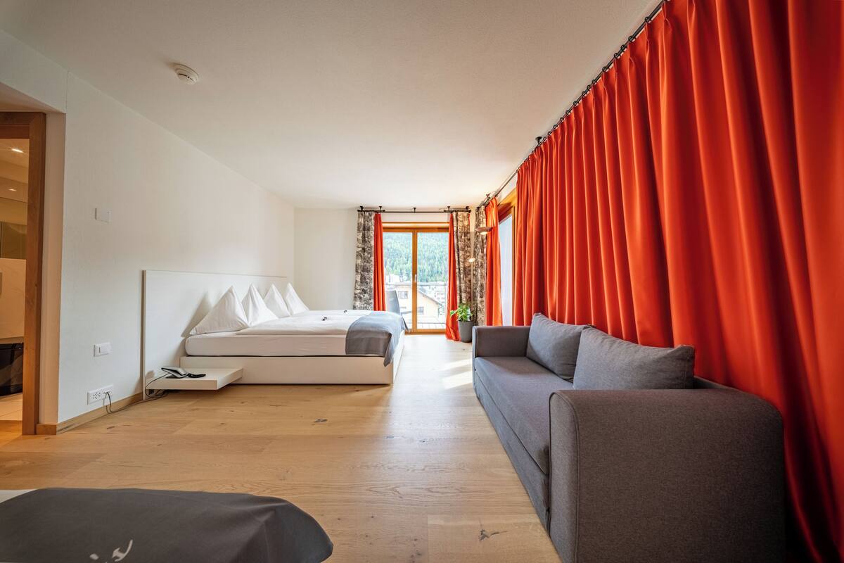 A modern bedroom with a bed, a sofa, and a large window with curtains.