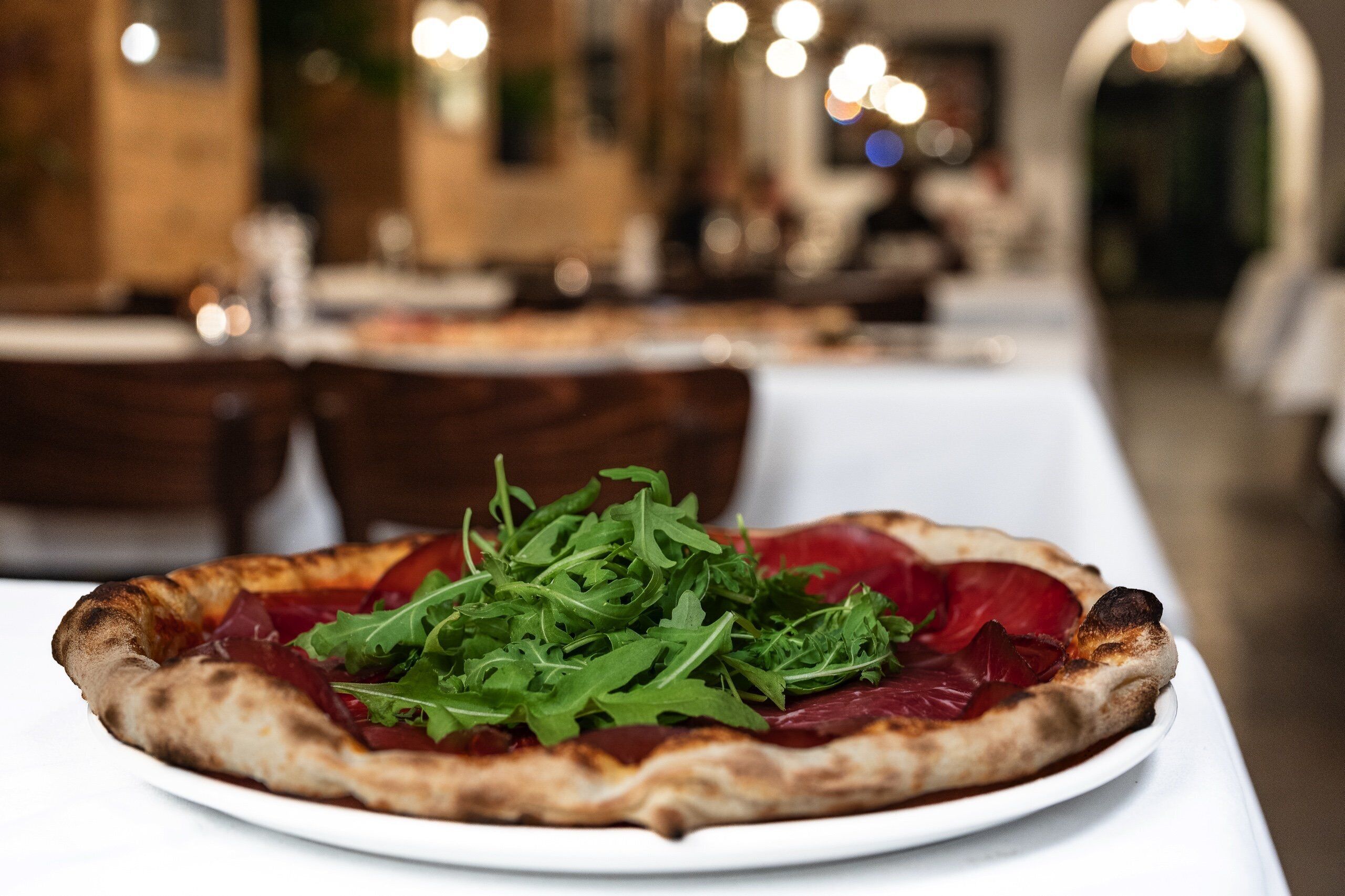 Una pizza con rúcula y remolacha sobre un plato blanco.
