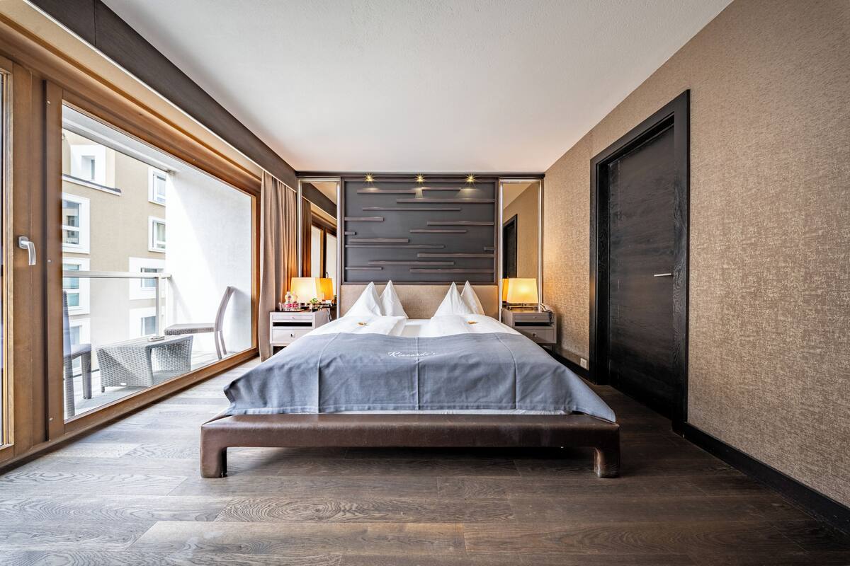 A modern hotel room with a large bed, a balcony, and a view of the city.