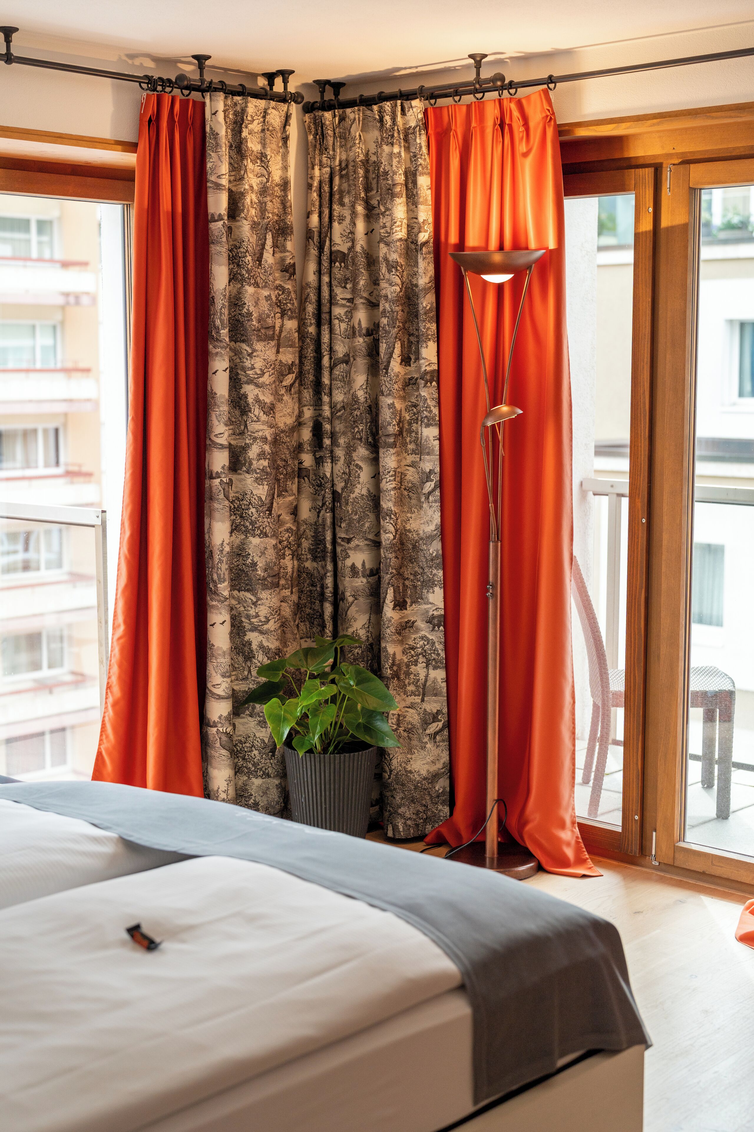 A bedroom with a bed, curtains, a potted plant, and a view through a window.