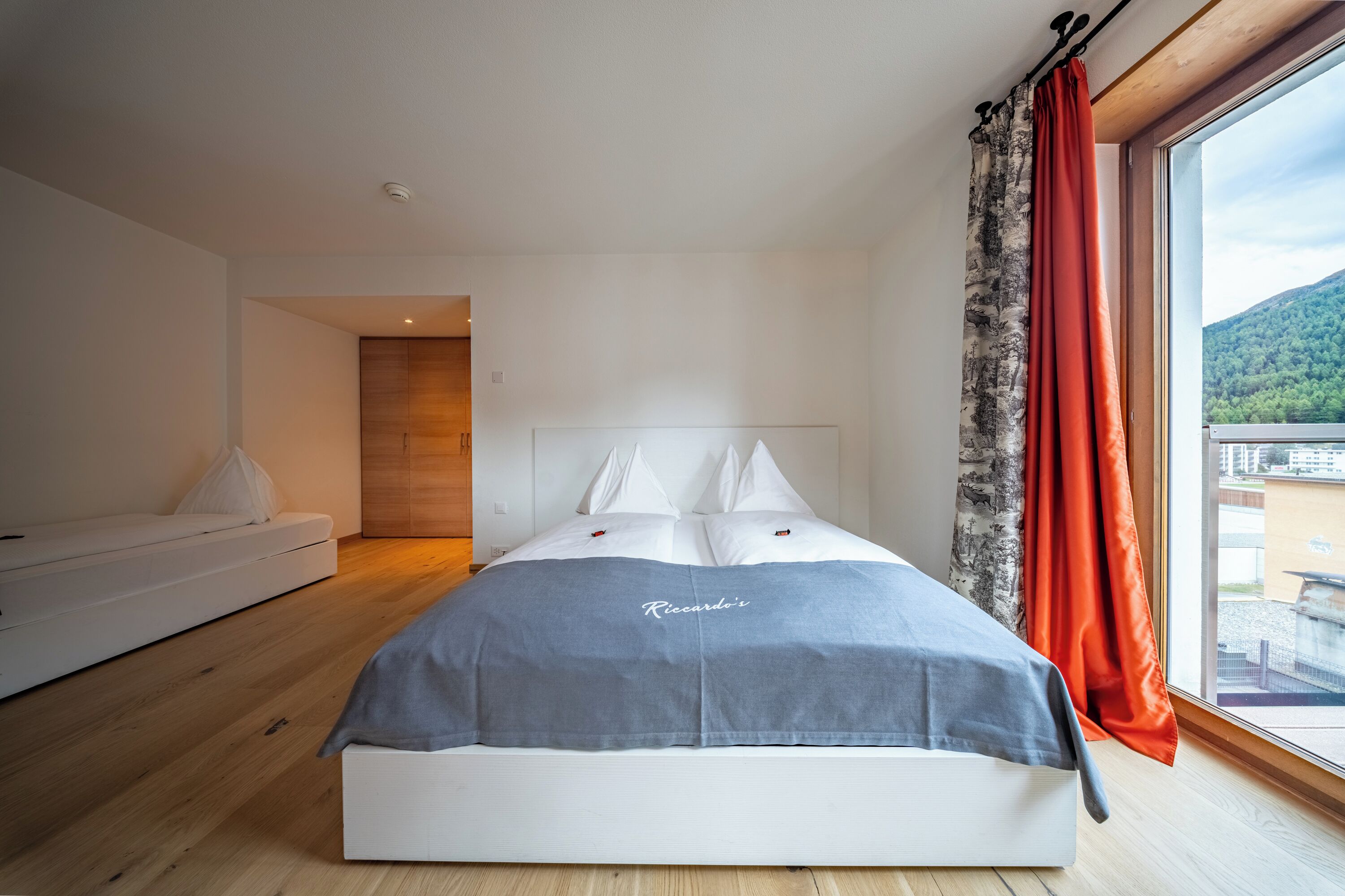 A modern bedroom with a large bed, a white sofa, and a view of a mountain through a window.
