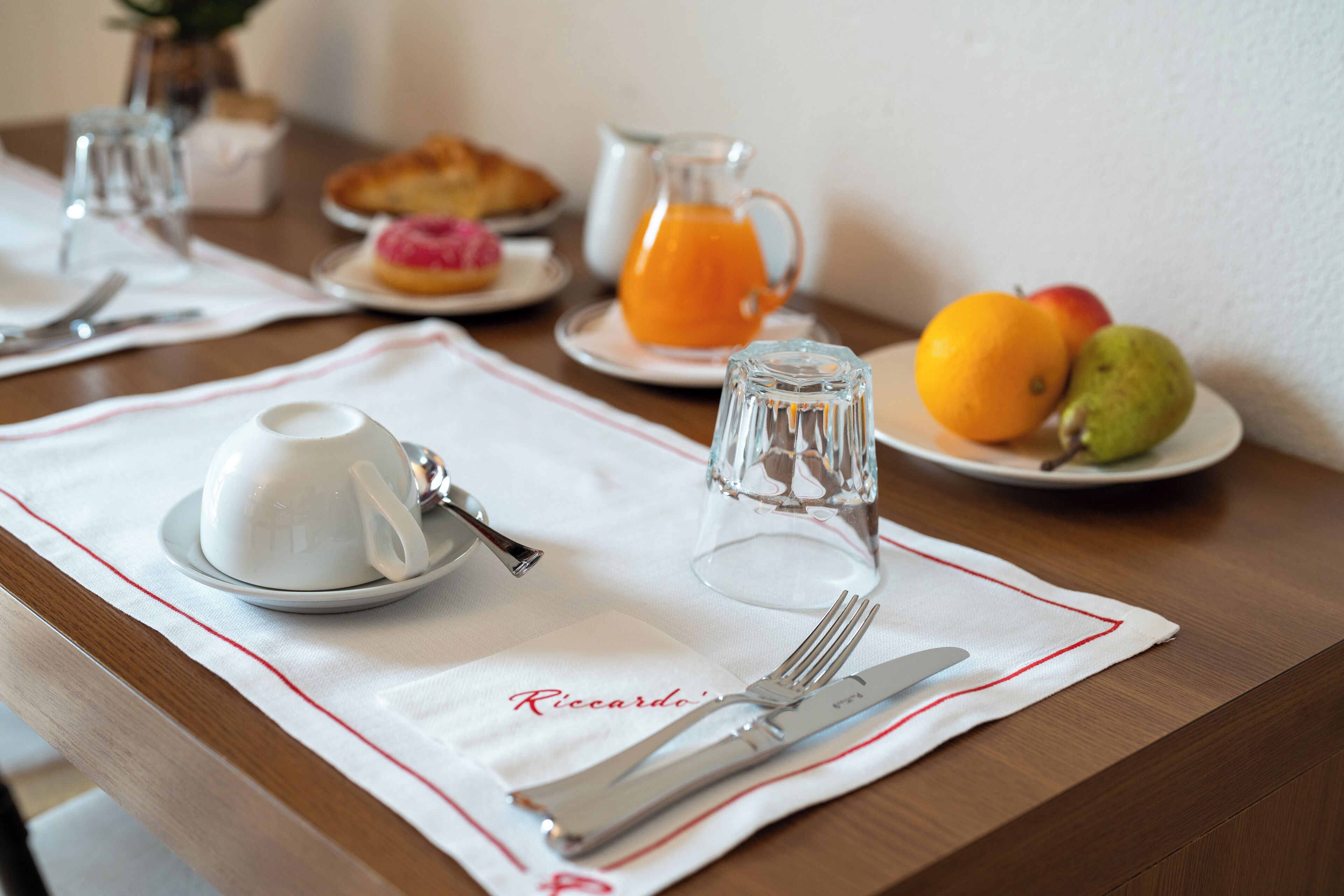 Un desayuno con mantel blanco, un plato de fruta, una jarra de jugo de naranja y una taza de café.