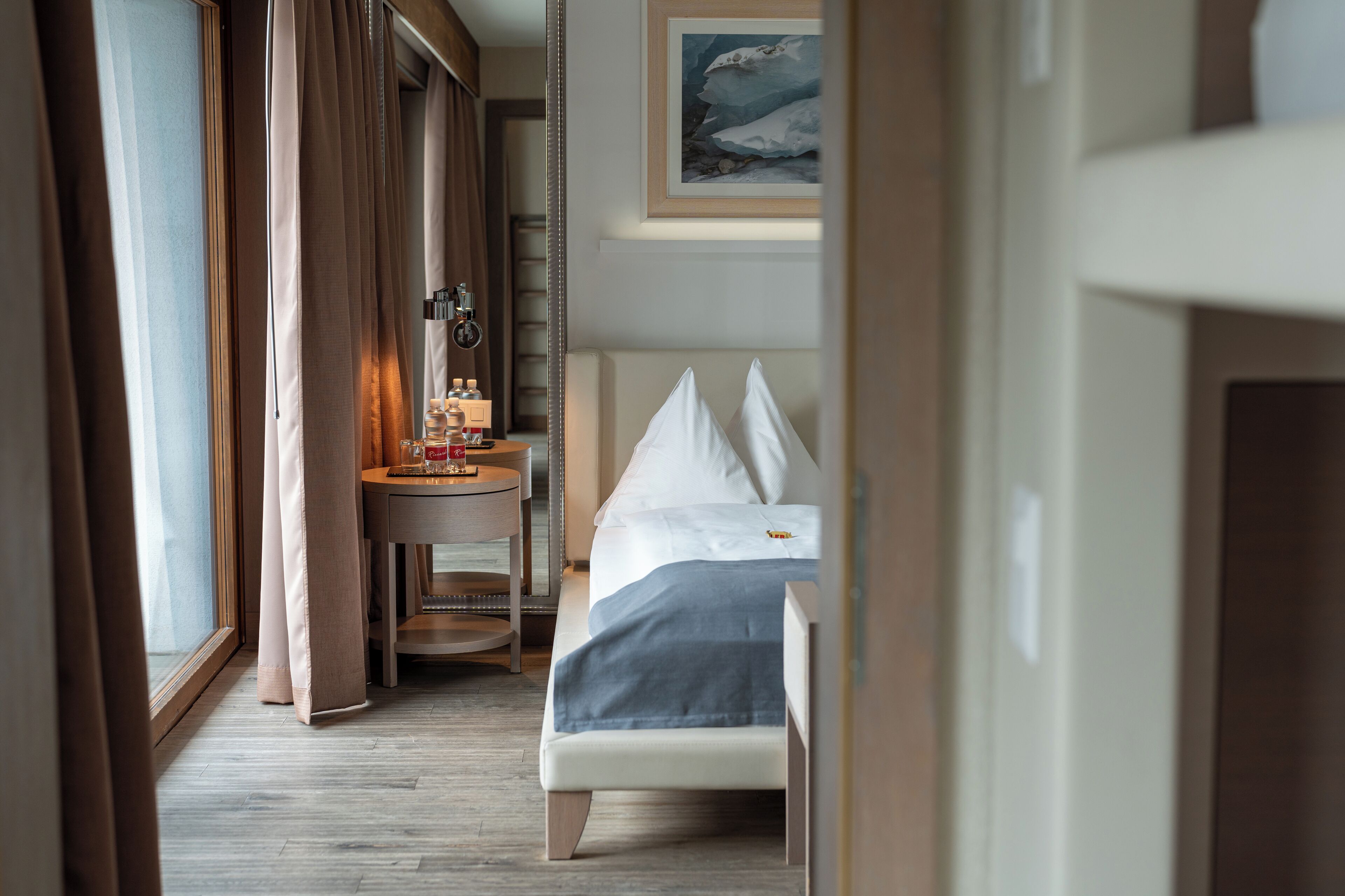 A hotel room with a bed, bedside table, and a window with curtains.
