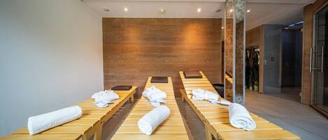 A modern spa room with wooden benches and towels, a wooden wall, and a glass door leading to a shower area.
