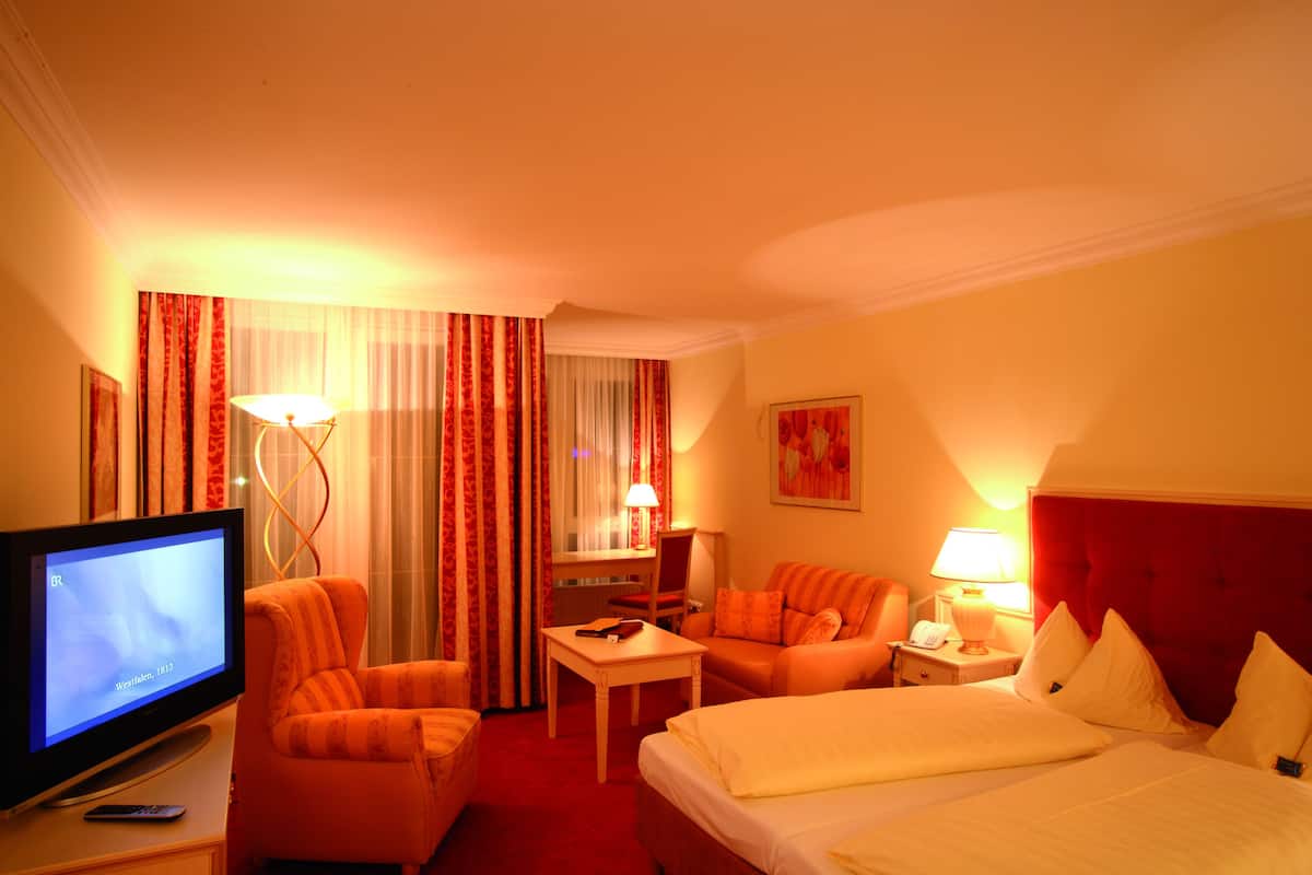 A hotel room with a television, two sofas, a bed, a desk, and a window with curtains.