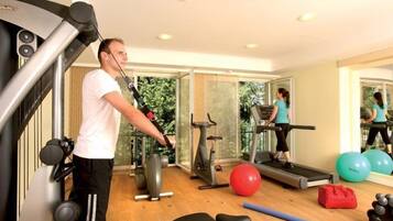 Un gimnasio con equipo de ejercicio, una cinta de correr y un espejo que refleja a una persona caminando.
