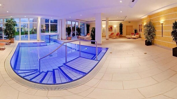 Ein moderner, überdachter Pool mit Glasbarriere, Liegestühlen und einer Treppe zu einer zweiten Ebene.