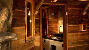 Interior rústico de una cabaña de madera con cocina, pared de piedra y ventana.