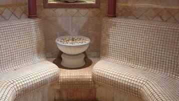 A bathroom with a tiled floor, a large window with a decorative stone, and two cushioned seating areas.