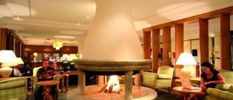 A lobby with a central fire feature, multiple seating areas, and a chandelier.