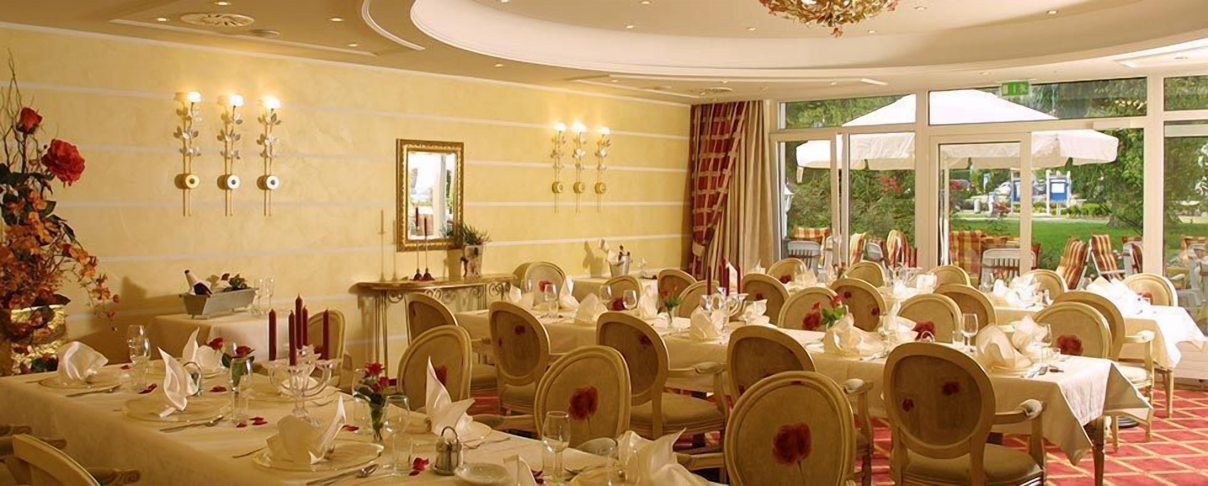 A formal dining room with multiple tables set for service, a large mirror, and a view of the outdoors through large windows.