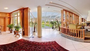 Eine großzügige Lobby mit einer zentralen Sitzecke, großen Fenstern und Blick ins Freie.