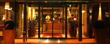 A hotel entrance with a glass door, a reception desk, and potted plants.