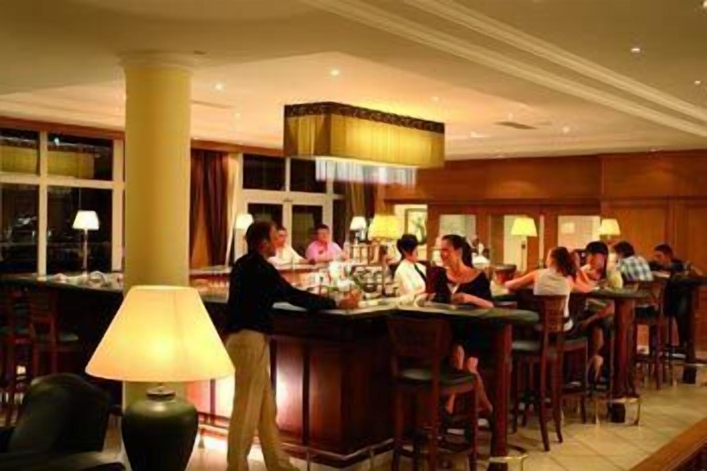 A bar area with multiple stools and tables, a bartender, and patrons seated.