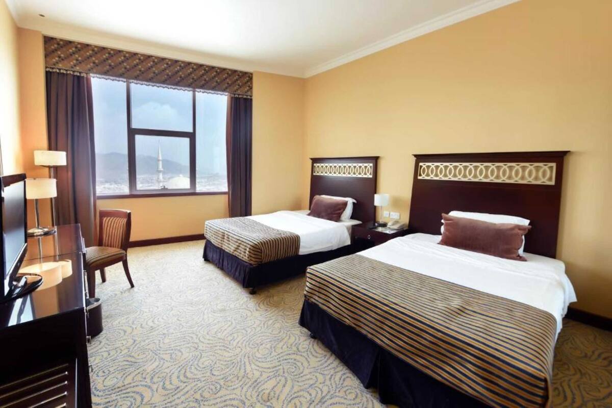 A hotel room with two beds, a desk, a chair, and a large window with a view.