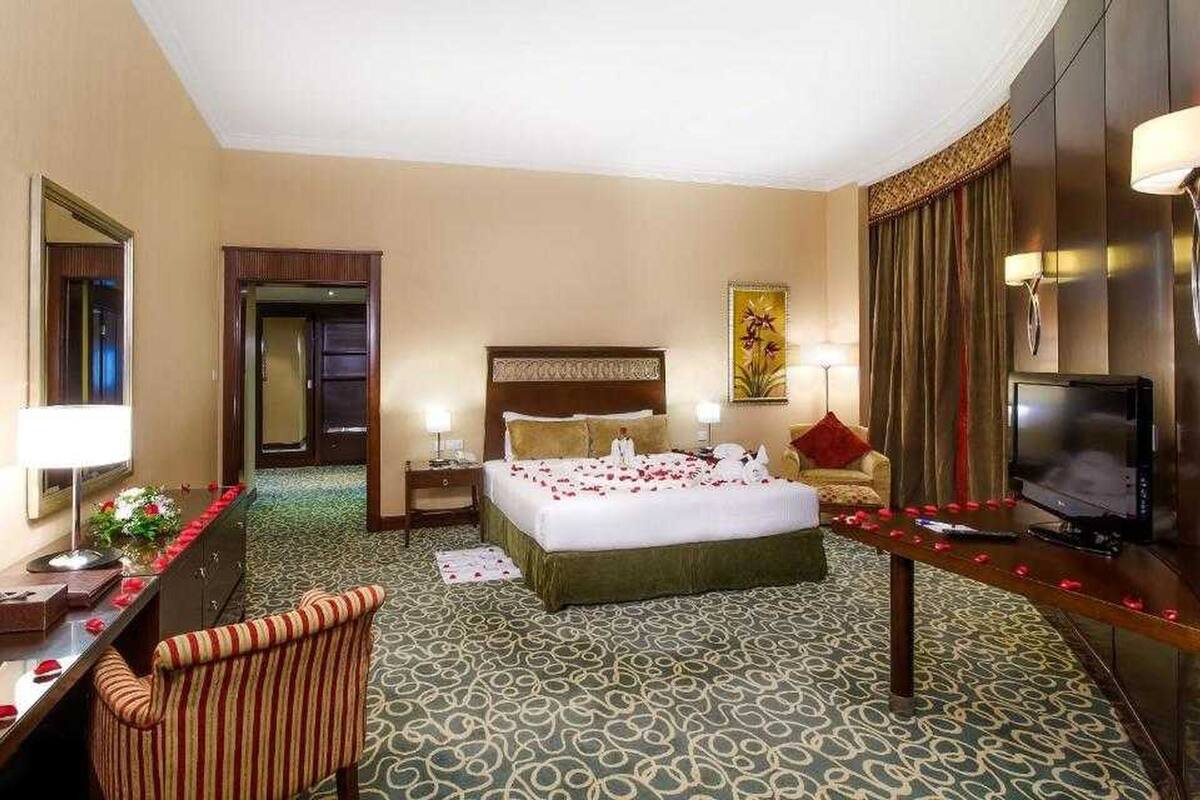 A hotel room with a large bed, a television, a desk with a lamp, and a chair.