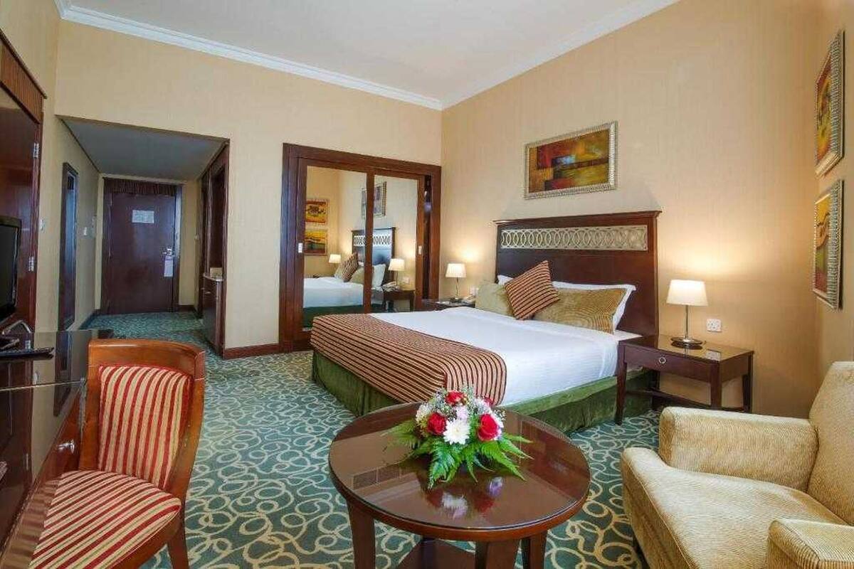 A hotel room with a large bed, a sitting area with a table and chairs, and a mirror on the wall.