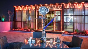 Un'area pranzo all'aperto con tavolo in vetro, sedie e hookah.