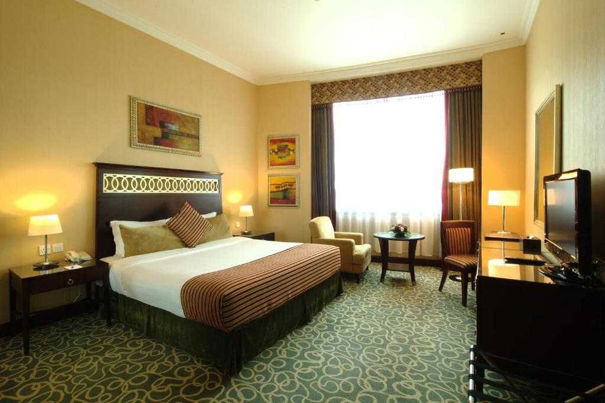A hotel room with a large bed, two chairs, a desk, and a television.