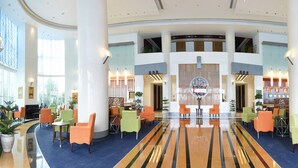 Un'ampia hall con una reception centrale, diverse zone relax e ampie finestre che lasciano entrare la luce naturale.