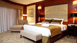 Una camera d'albergo con un letto grande, un divano, una panca e due comodini con lampade.