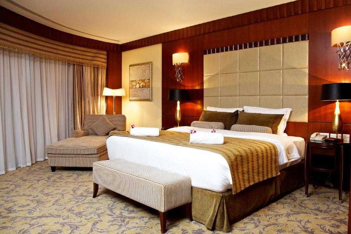 A hotel room with a large bed, a sofa, a bench, and two bedside tables with lamps.