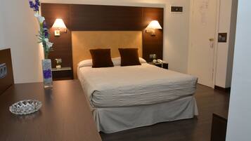 Una habitación de hotel con una cama grande, dos lámparas de noche, una mesita de noche, un jarrón con flores y un cabecero de madera.