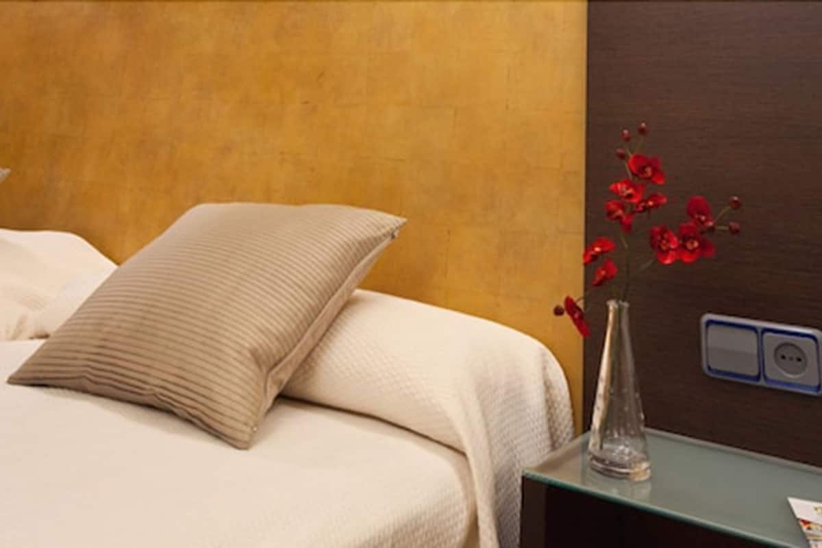 Een hotelkamer met een bed, een nachtkastje met een vaas rode bloemen, en een nachtkastje met een stopcontact.