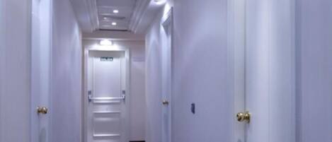 A long, narrow hallway with white walls and doors, leading to a room at the end.