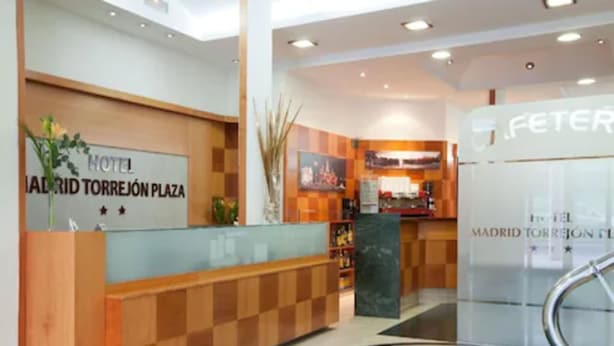 Ein Hotel-Empfangsbereich mit Check-in-Schalter, Rezeption und einer Glaswand mit einem Logo.