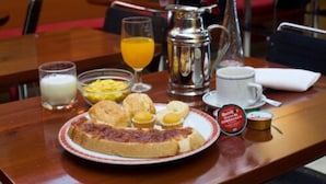 Ein Frühstückstisch mit einem Teller Essen, einer Kaffeekanne, einem Glas Orangensaft und einer Milchglasse.