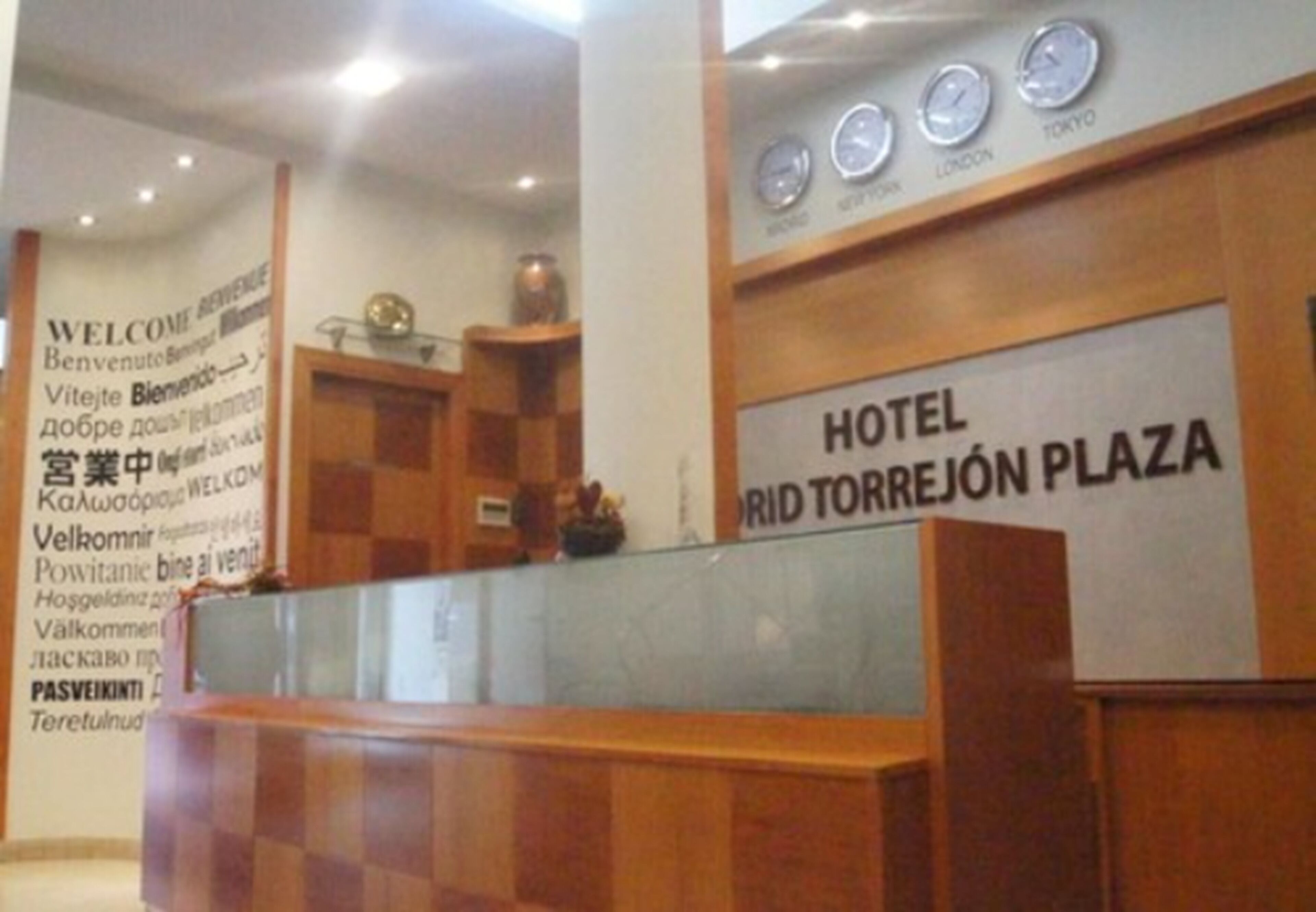A reception desk with a sign reading "HOTEL RÍD TORREJÓN PLAZA" and clocks displaying times for London and Tokyo.