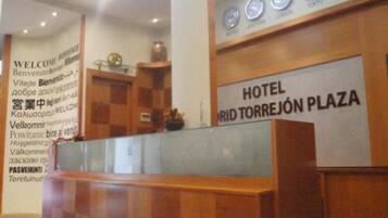 A reception desk with a sign reading "HOTEL RÍD TORREJÓN PLAZA" and clocks displaying times for London and Tokyo.