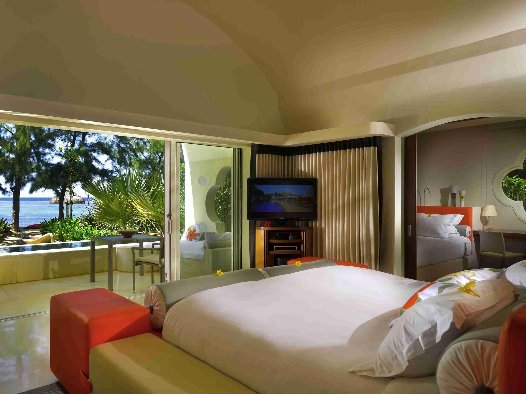 A hotel room with a large bed, a TV, a balcony with a view of the ocean, and a dining area.