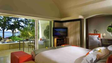 A hotel room with a large bed, a TV, a balcony with a view of the ocean, and a dining area.