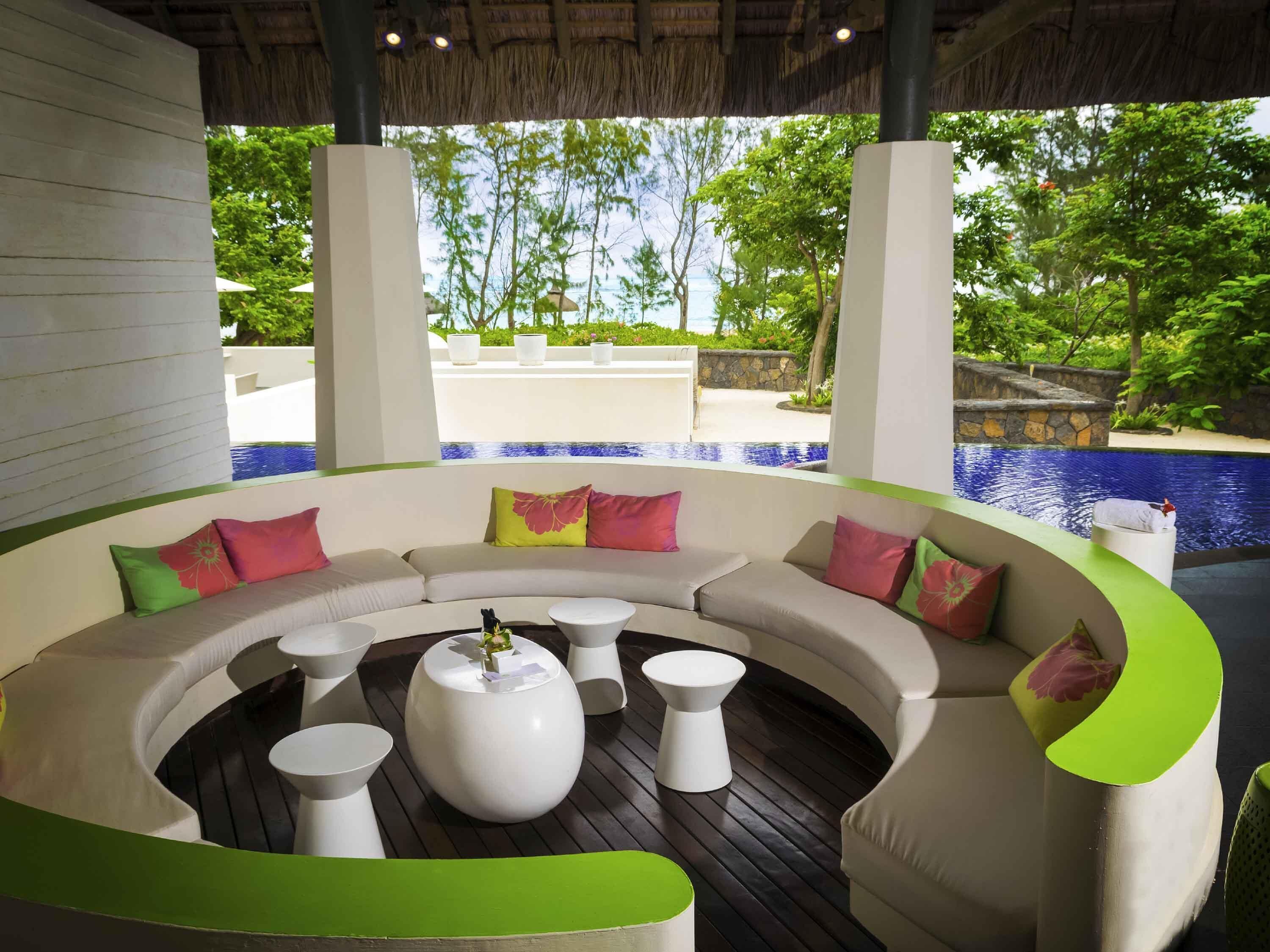 A modern outdoor seating area with a curved sofa, white coffee tables, and colorful cushions.