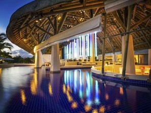 Un área de piscina con una estructura de techo de paja, asientos y una piscina reflectante.
