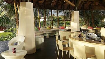 Un espacio lounge moderno al aire libre, con una disposición de asientos curva, una barra con varias botellas y una estructura de techo de paja.