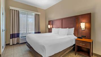 Una habitación de hotel con una cama grande, una mesita de noche con lámpara y una ventana con cortinas.