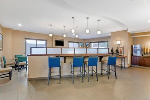 A bar area with multiple stools, a counter, and a television screen. - Comfort Suites Blythe (Blythe)