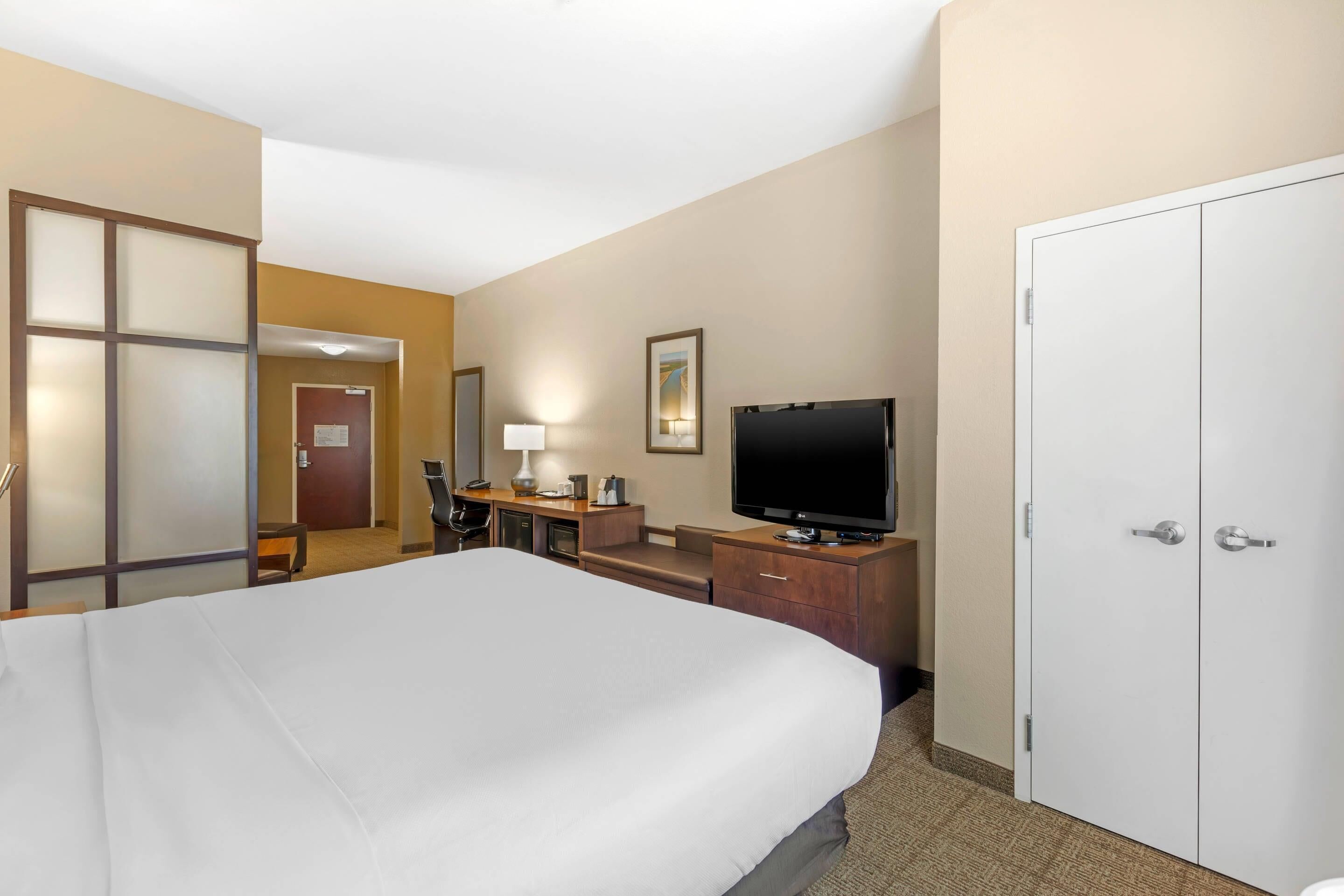 A hotel room with a large bed, a desk with a computer, a television, and a wardrobe.