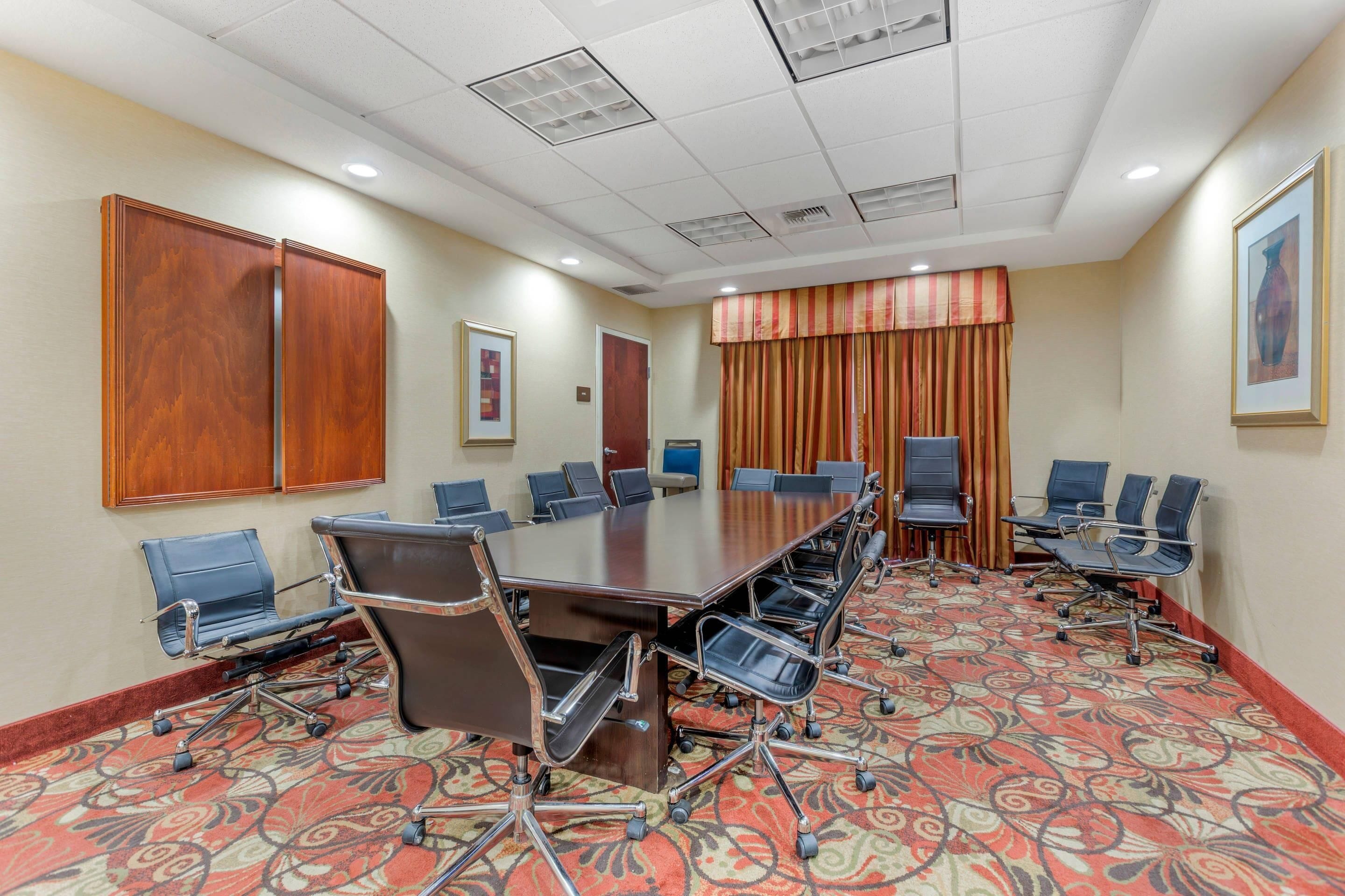 A conference room with a long table, chairs, and a patterned carpet.